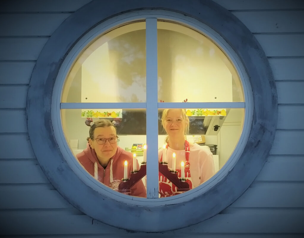 Minna ja Jaana kurkkaavat Kesäharjun ikkunasta kynttelikön takaa jouluisasti.
