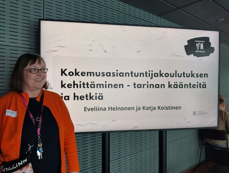 Kuvassa iloinen Sirpa ja tapahtuman kyltti.