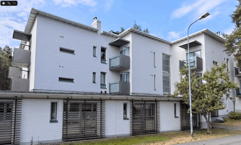 Moderni, vaaleaksi maalattu asuinrakennus, jossa on parvekkeita ja ympärillä vihreitä puita.