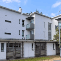 Moderni, vaaleaksi maalattu asuinrakennus, jossa on parvekkeita ja ympärillä vihreitä puita.