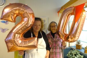 Kaksi henkilöä pitää kädessään suuria vaaleanpunaisia ilmapalloja, joissa on numerot 2 ja 0.