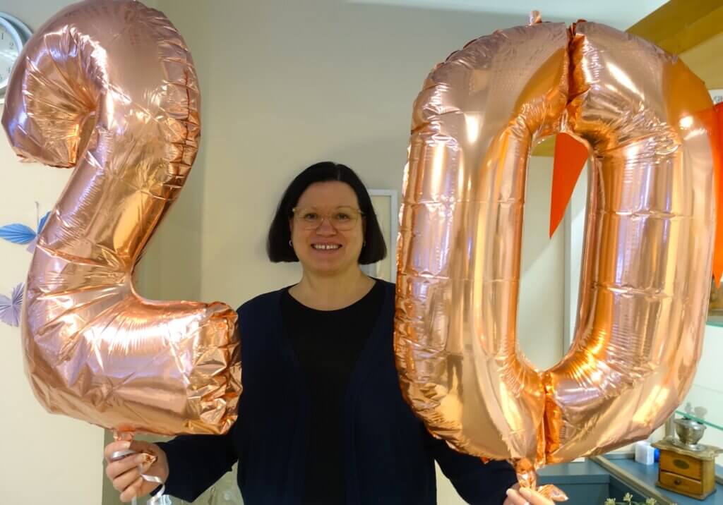 Nainen pitää käsissään suuria, vaaleanpunaisia ilmapalloja, joissa on numerot 2 ja 0.