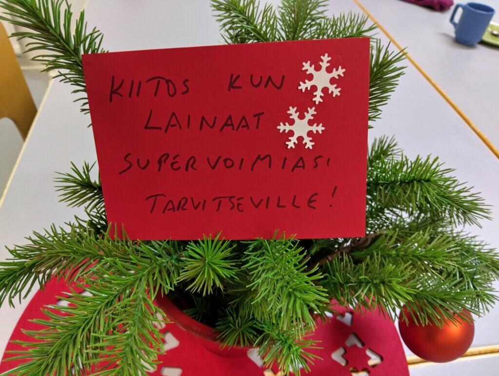 Pöydällä on joulupuu, jossa on punainen kortti, jossa lukee kiitos lainatuista supervoimista.