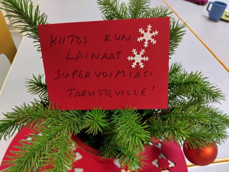 Pöydällä on joulupuu, jossa on punainen kortti, jossa lukee kiitos lainatuista supervoimista.