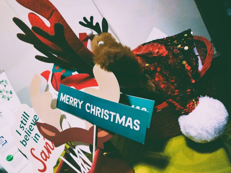 Koristeellinen kori, jossa on jouluteemaisia esineitä, kuten "MERRY CHRISTMAS" -kyltti ja joulupukin hattu.