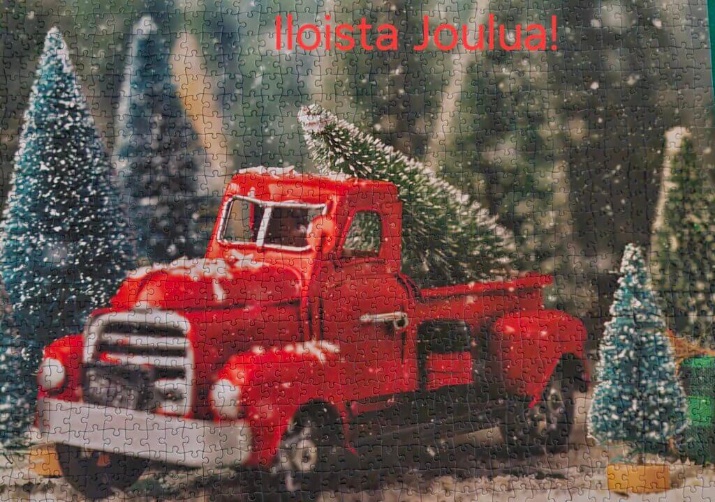 Punainen rekka, jossa on joulukuusi, ja taustalla lumisia puita sekä teksti "Iloista Joulua!