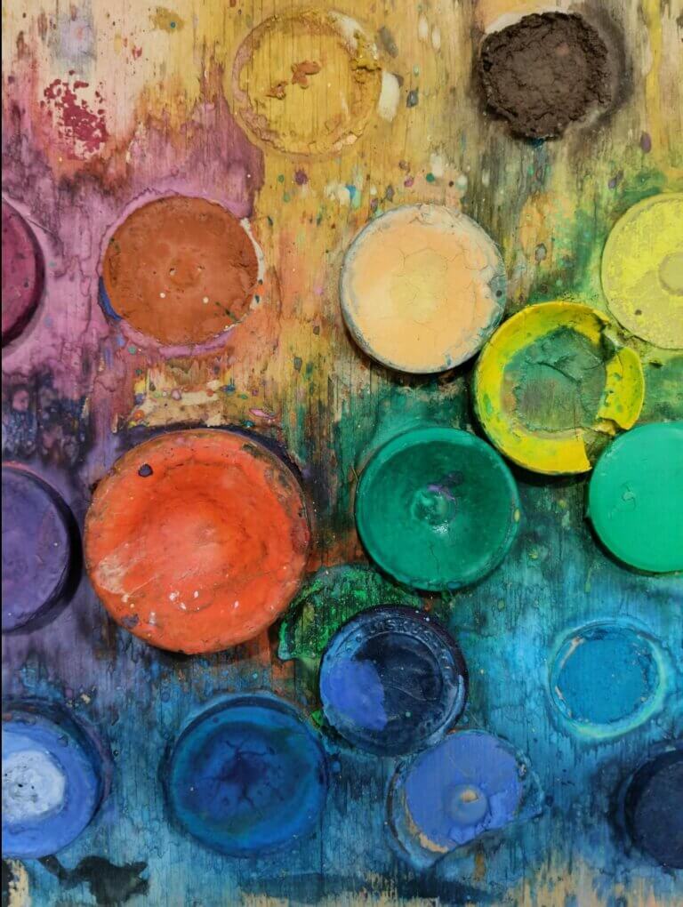 Väripaletti, jossa on monivärisiä maaleja ja tahroja puupinnalla.