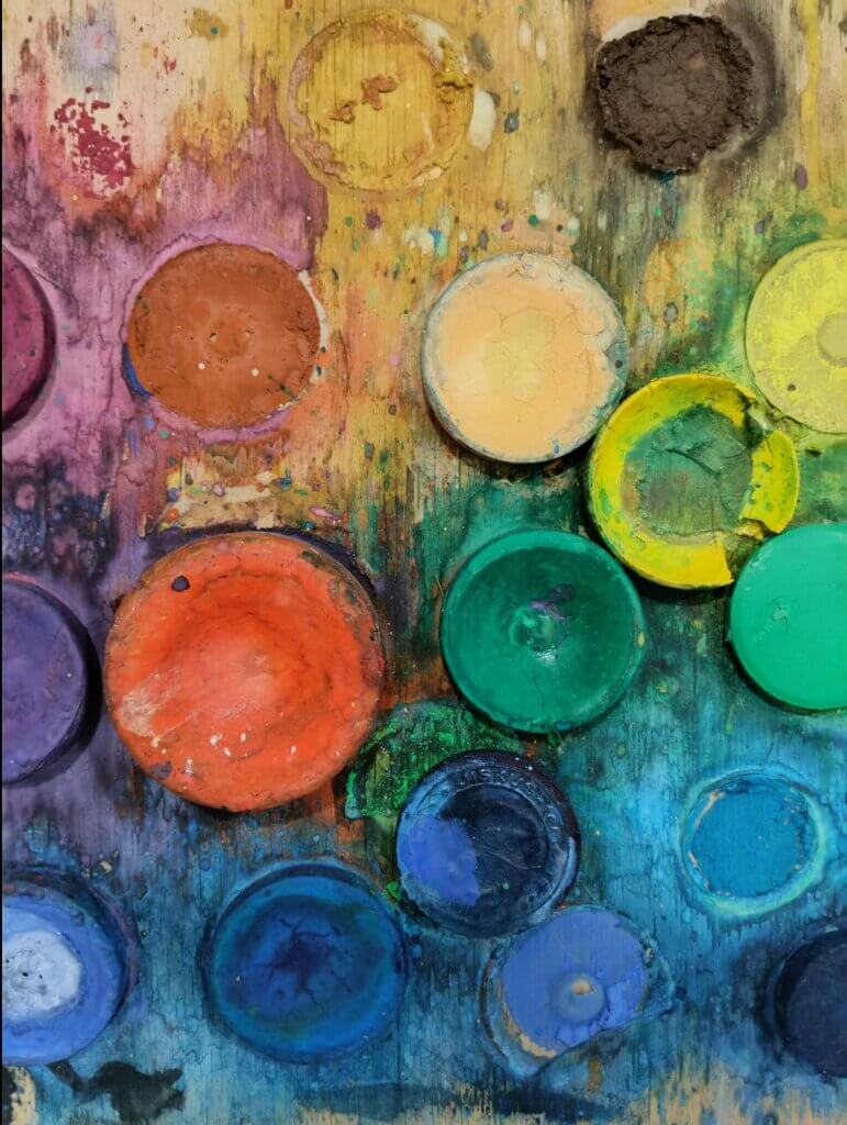 Väripaletti, jossa on monivärisiä maaleja ja tahroja puupinnalla.