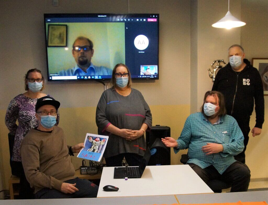 Kuudesta maskipäisestä henkilöstä koostuva ryhmä esittelee haikukirjaa videopuhelun aikana.