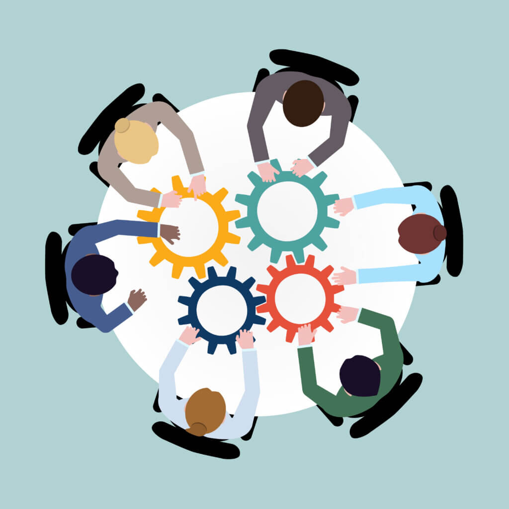 Yhdeksän henkilöä työskentelee yhdessä pyöreällä pöydällä, jossa on värikkäitä hammasrattaita.