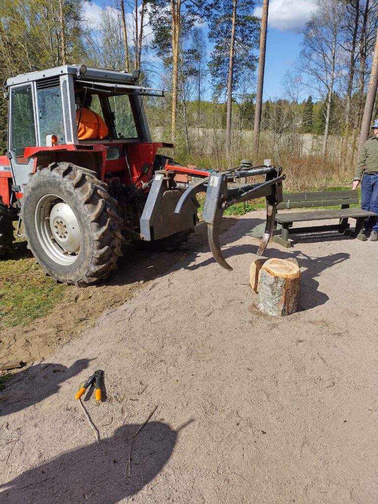 Traktori, jossa on puun nostoväline, on pysähtynyt puunrunkojen lähelle metsäisessä ympäristössä.