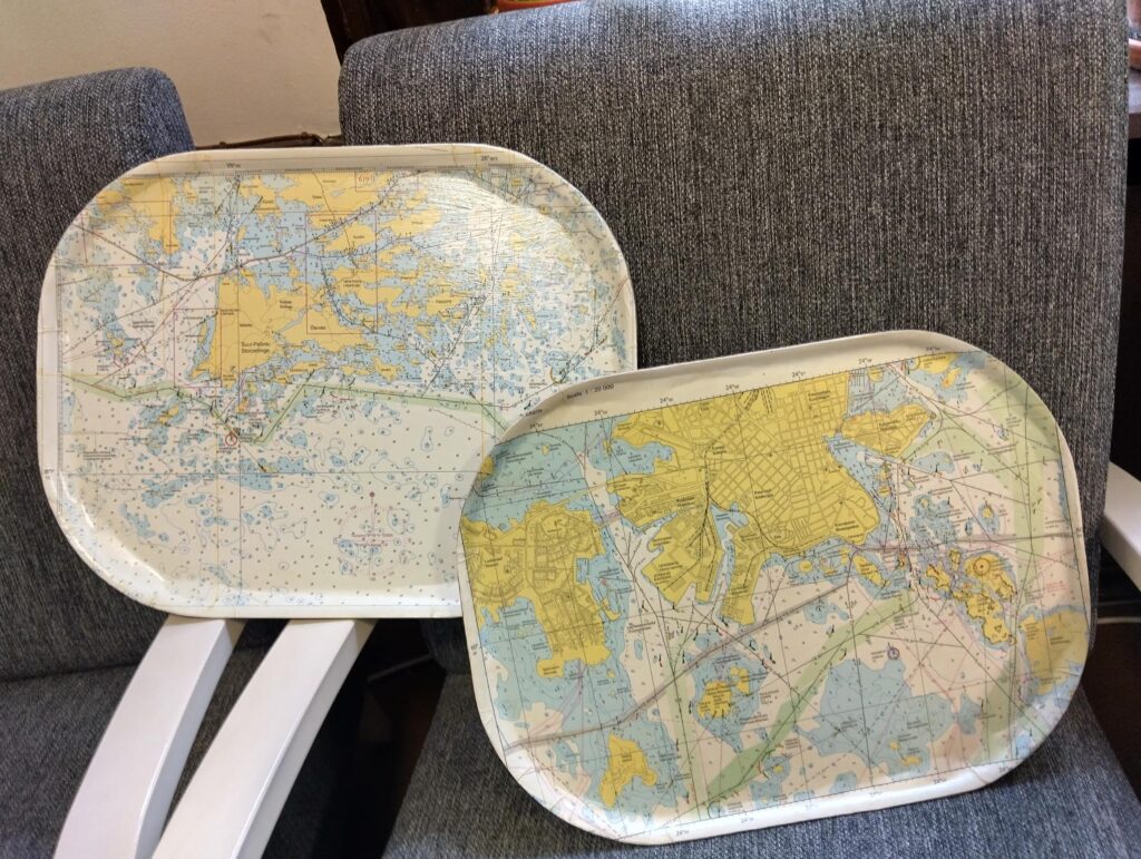 Tarjottimilla on vanhoja merikarttoja, jotka on pinnoitettu eri väreillä ja kuvioilla.