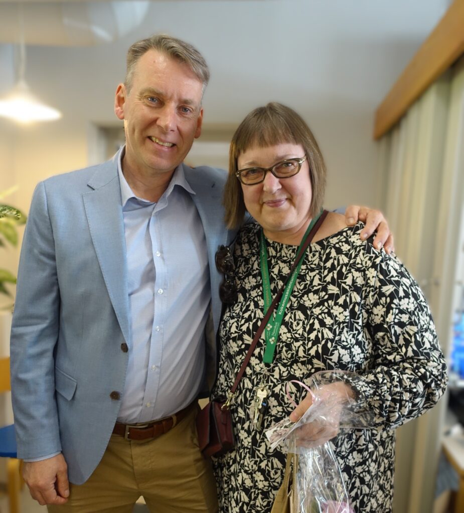 Kaksi henkilöä hymyilee yhdessä, toinen heistä pitää kädessään lahjaa.