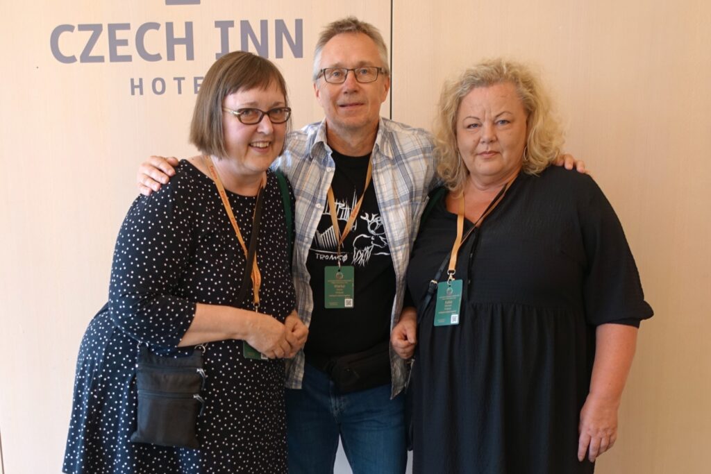 Kolme henkilöä seisoo yhdessä hotellin taustalla, jokaisella on nimikortti kaulassa.