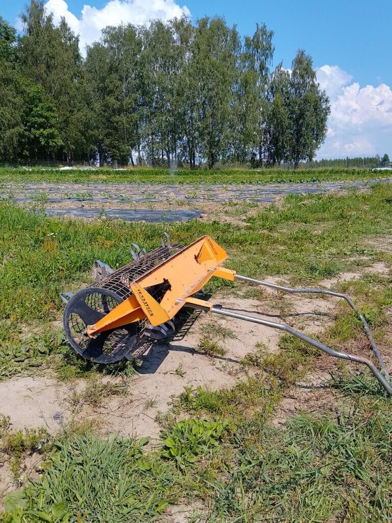 Kuva maataloustarvikkeesta, joka on asetettu nurmialueelle kirkkaan sinisen taivaan alla. Taustalla on rivi puita.
